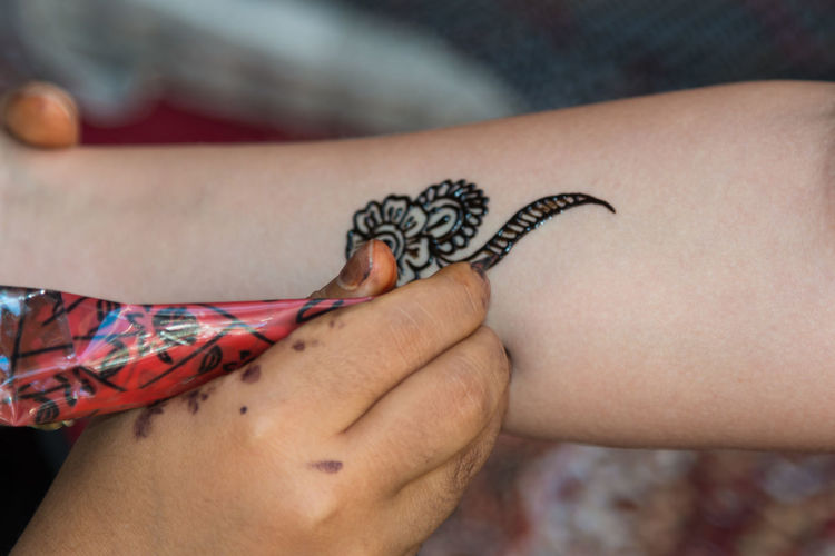 Cropped hand making henna tattoo on forearm
