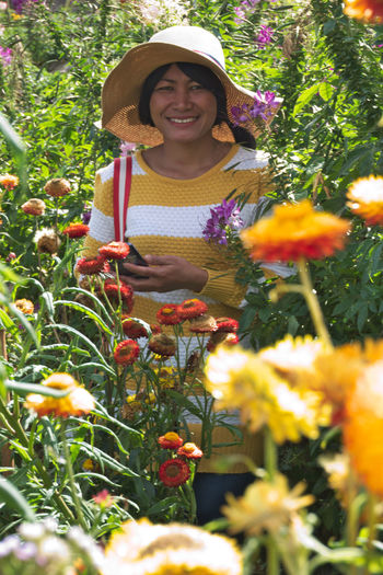 Portrait of smiling woman standing by flowering plants