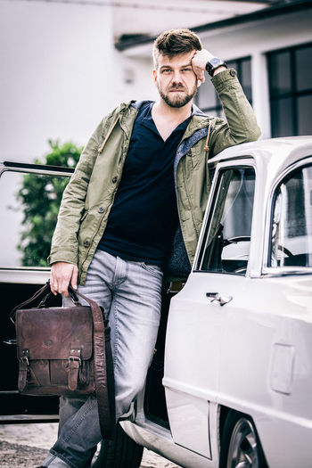 Portrait of man holding briefcase while leaning on car