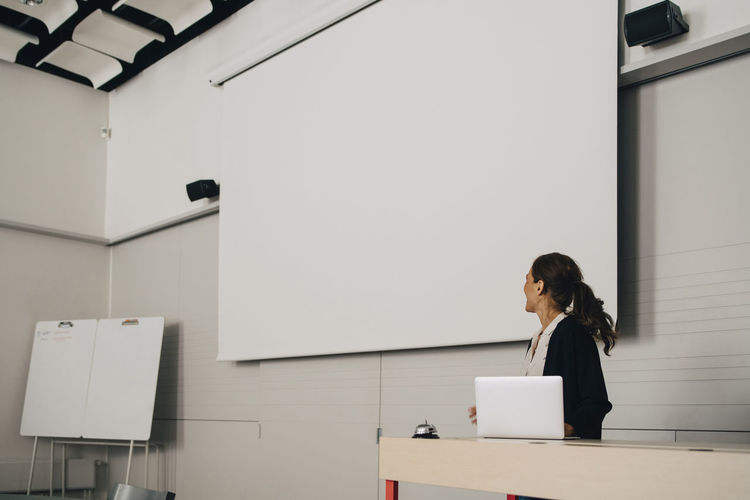 Businesswoman giving presentation while looking at blank projection screen at creative office
