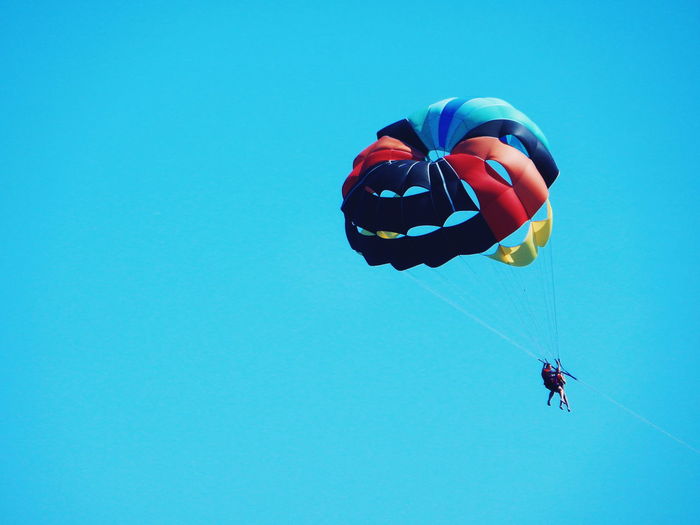Low angle view of parachuting against clear blue sky