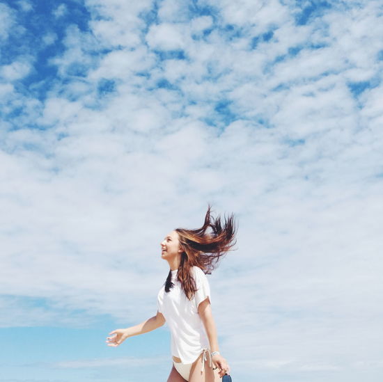 Smiling young woman standing against cloudy sky
