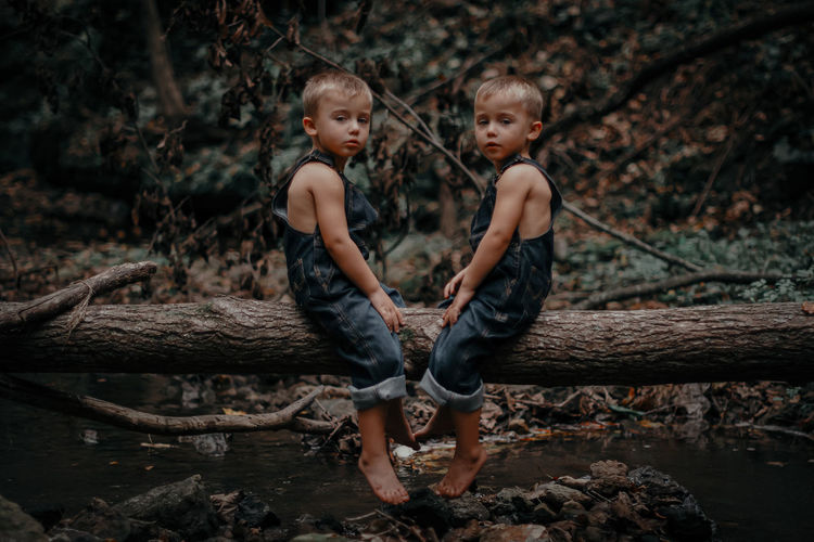 Full length of twin siblings sitting on wood