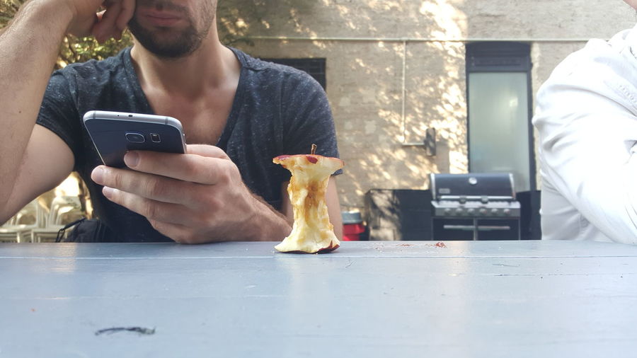 Midsection of man using phone with eaten apple on table