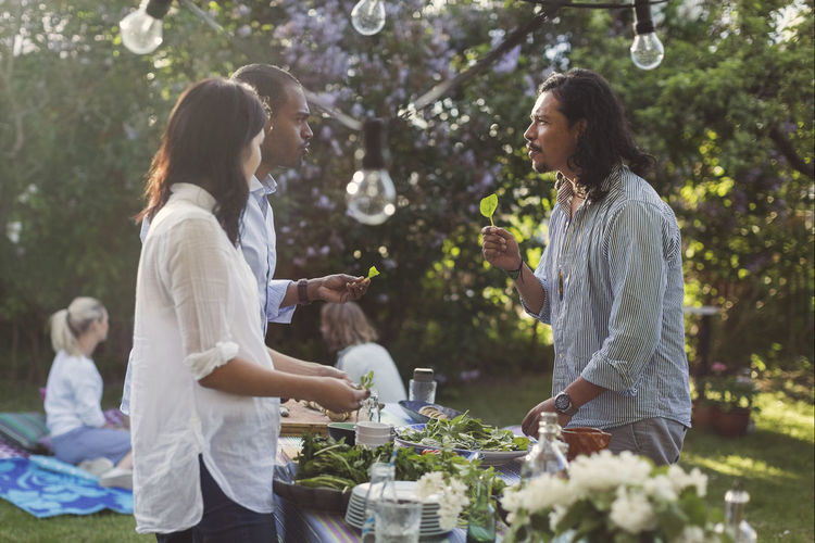 Multi-ethnic friends talking while cutting vegetables in backyard during summer party