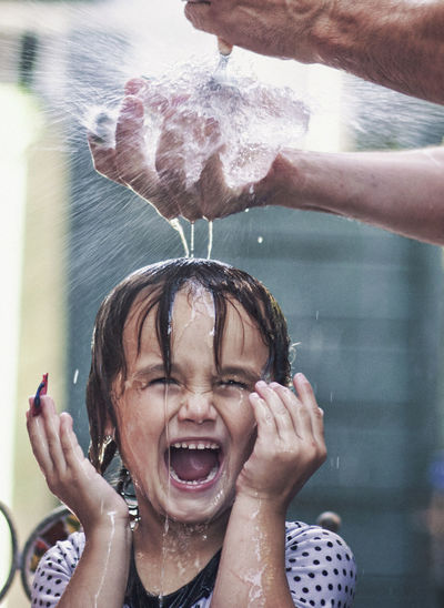 Cropped hand of father bursting water bomb over happy daughter head