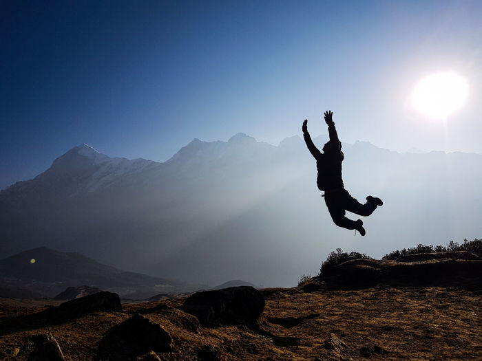 Silhouette man jumping on mountain against sky