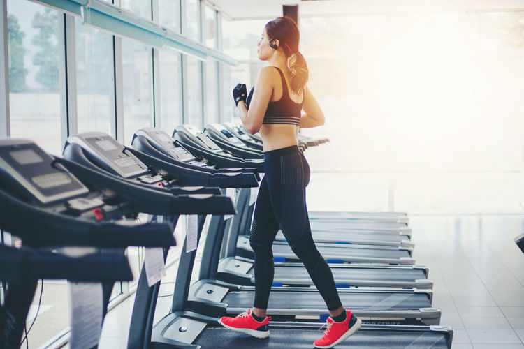 Side view of young woman walking on treadmill at gym