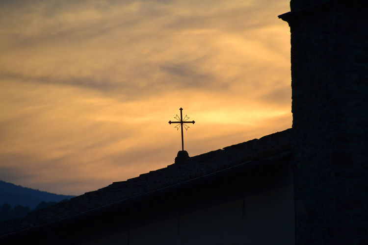 Low angle view of weather vane and cross against sky at sunset