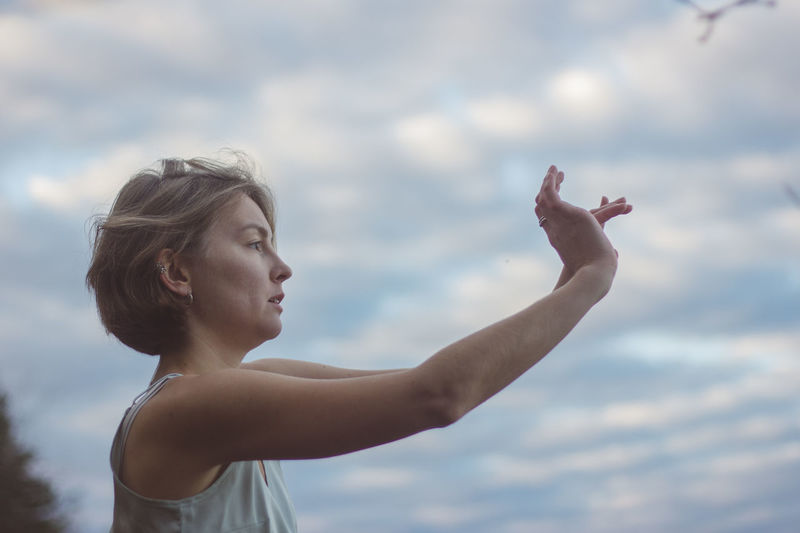 Portrait of woman with arms raised against sky
