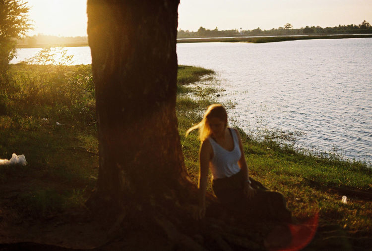 Woman sitting on tree trunk by water