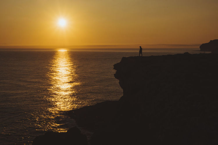 Young man stands at the cliff by the seaside watching sunrise, cantabria, spain