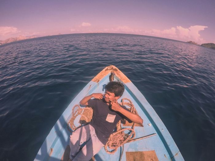 High angle view of young man looking away while sitting in boat on sea against sky during sunset