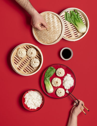 Chinese dinner table with steamed pork baozi dumplings, pak choi, and rice, on a red background.