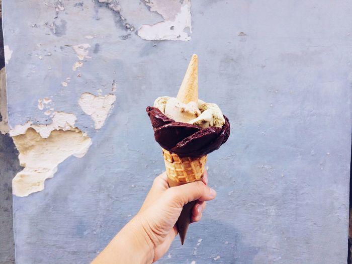 Close-up of hand holding ice cream cone against damaged wall