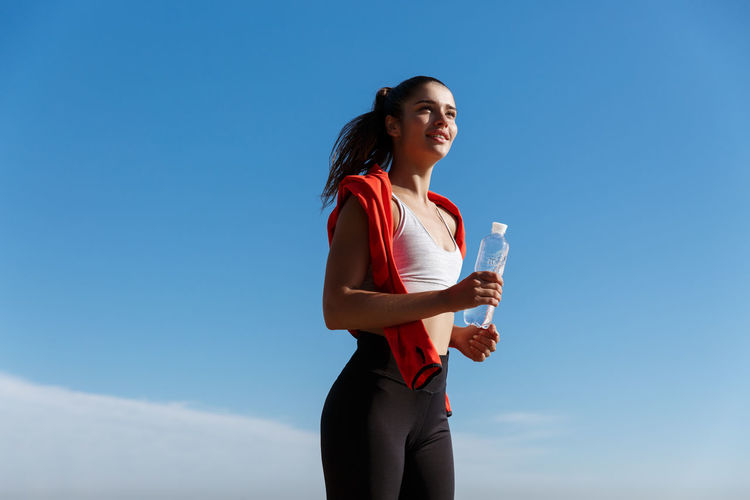 Low angle view of woman jogging against clear sky