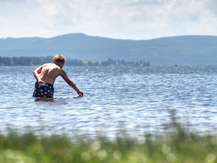 Boy stay in cold lake with water under knee and test temperature. cold spring day for swim.