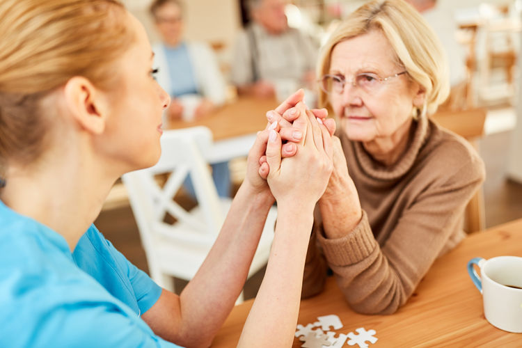 Female caregiver consoling senior woman in nursing home
