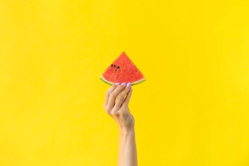 Close-up of hand holding lemon against yellow background