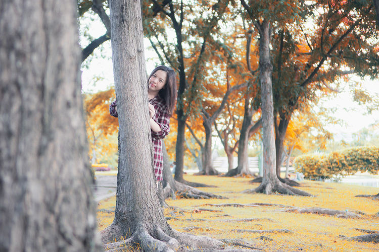 Portrait of young woman standing by tree trunk during autumn
