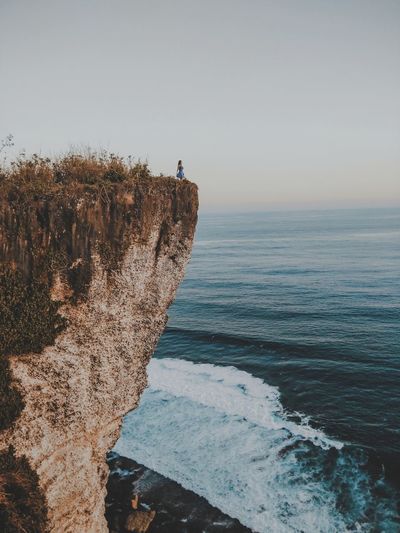 Woman standing on cliff against sea during sunset
