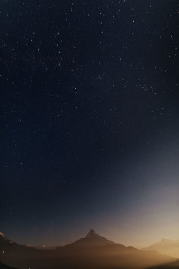 View of a mountain lit by moonlight at night against a starry sky
