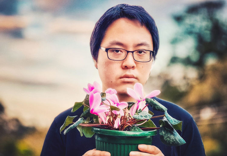 Portrait of young man holding pink flowering cyclamen plant.