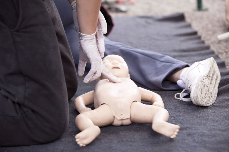 Midsection of paramedics performing cpr on baby mannequin