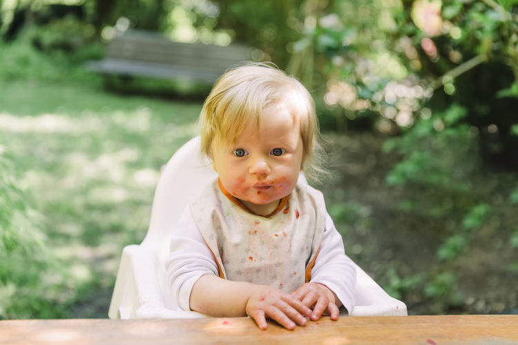 Portrait of cute baby girl sitting by table outdoors