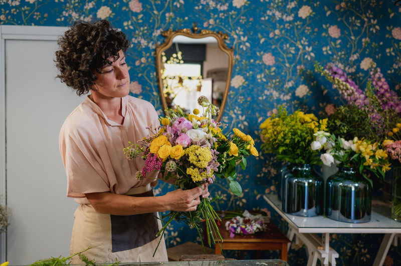 Female florist creating flower bouquet while working at table in floral store