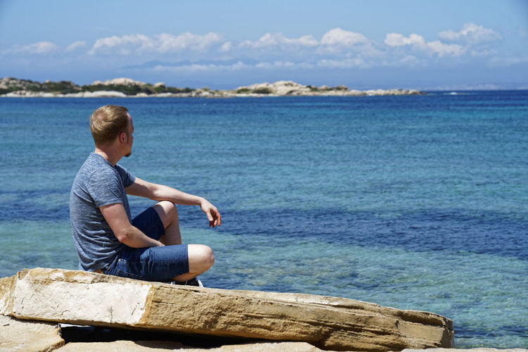 Man sitting by sea against sky