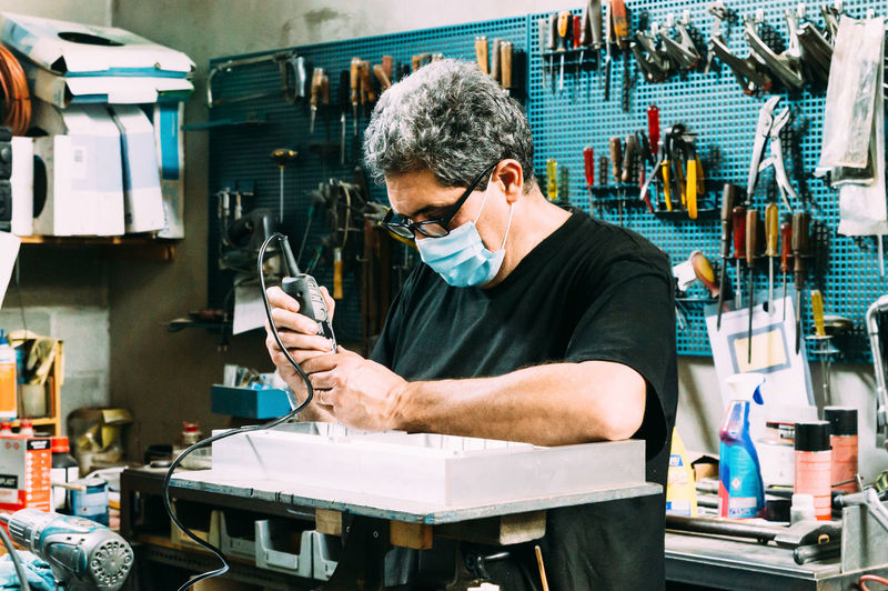 Focused craftsman wearing protective medical mask and eyeglasses soldering in modern equipped craftsmanship