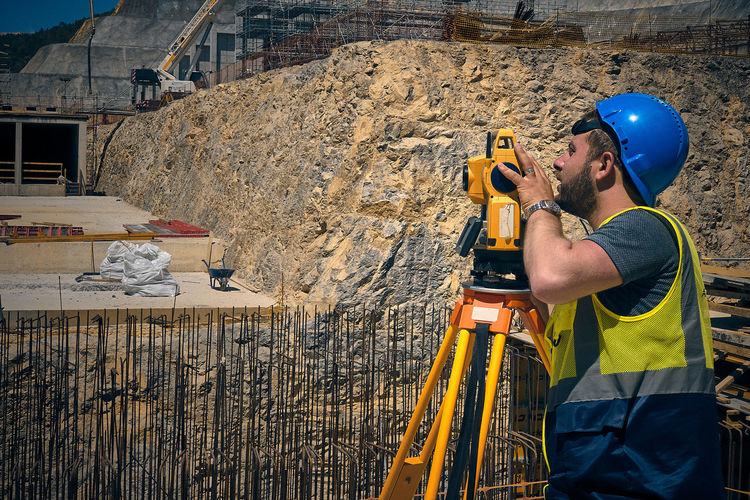 Land surveyor stands by theodolite on a tripod against construction site. topographic measurements 