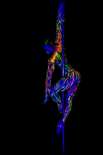 Full length of woman wearing neon clothing doing pole dance against black background