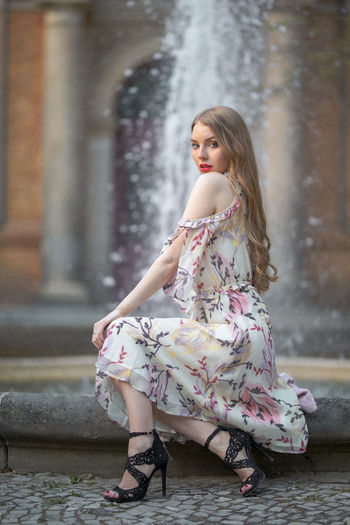Portrait of beautiful young woman sitting against fountain in city