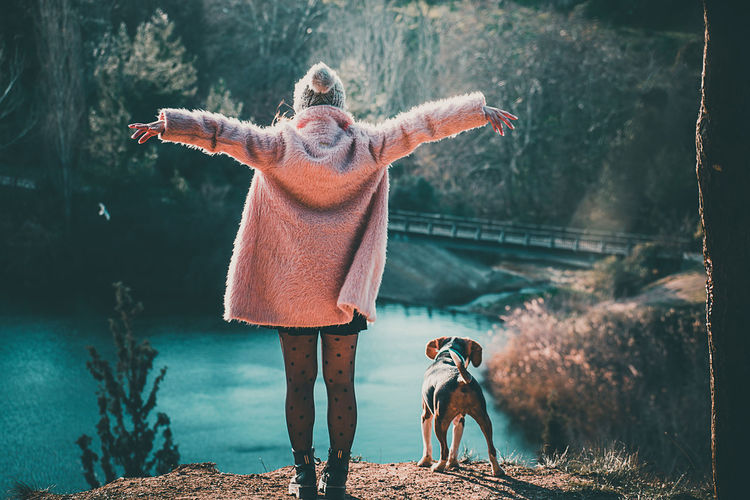 Rear view of woman with dog standing at lake