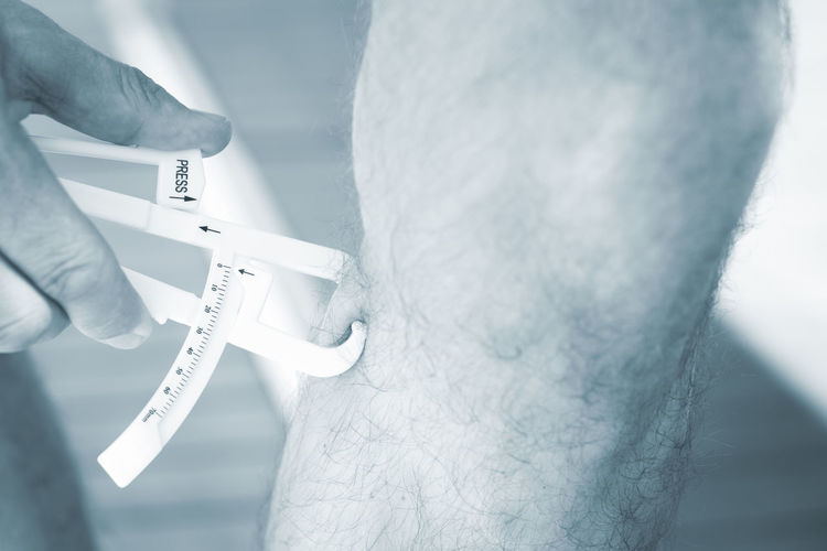 Midsection of man checking leg fat with caliper