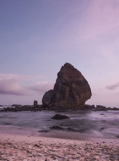 Rock formation on beach against sky during sunset