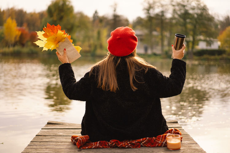 Woman in a red beret reading book on wooden pontoon. autumn season.