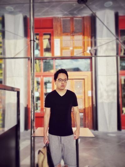 Portrait of young man standing outside storefront under mirrored reflection.