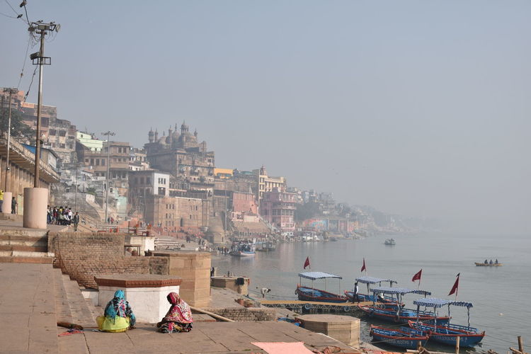 People on ganges by city against sky