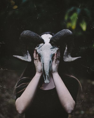 Woman covering face with animal skull while standing on field