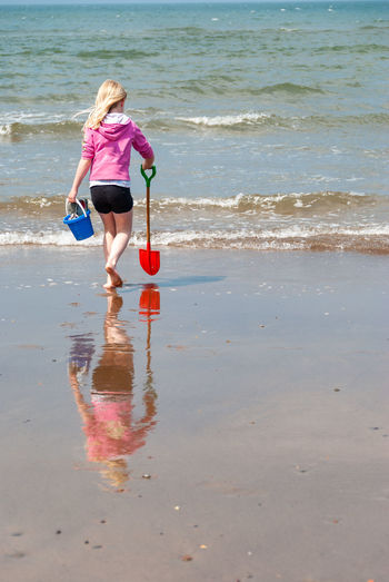 Rear view of girl with toys walking at beach during sunny day
