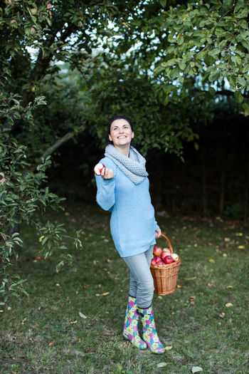 Happy beautiful woman holding apple with basket at orchard