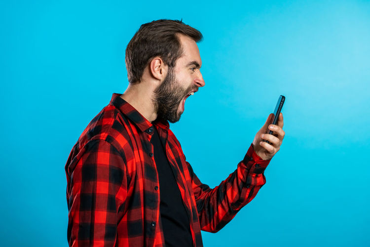 Low angle view of man using mobile phone against blue background