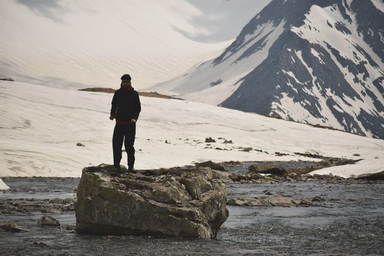 Full length of man standing on rock against snowcapped mountains