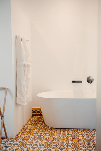Interior of modern light bathroom with white oval bathtub and walls and traditional ornamental azulejo tiled floor