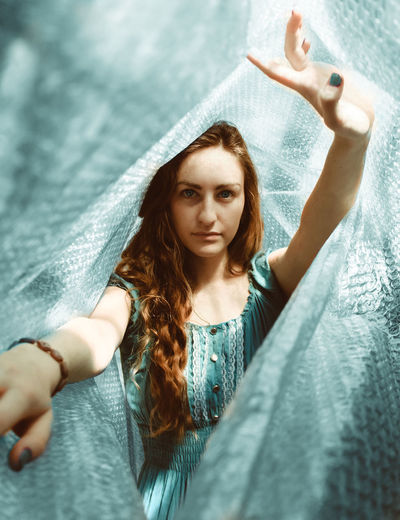 Portrait of beautiful young woman with arms raised standing amidst bubble wrap