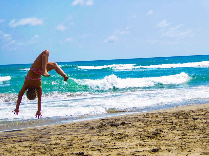 Full length of girl jumping upside down at beach against sky