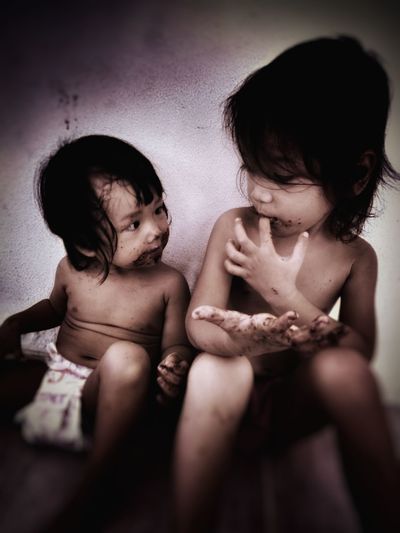 Cute shirtless siblings with messy hands looking at each other against wall